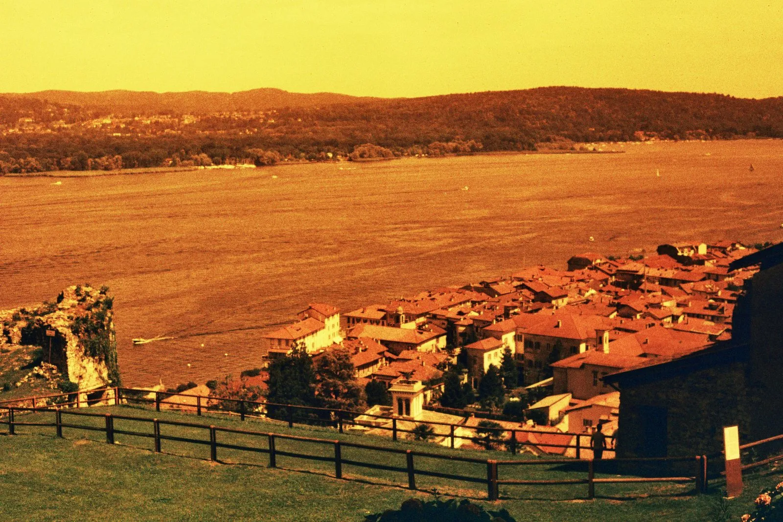 Un paese sul lago visto dall’alto, tutto in toni di rosso, arancione e giallo